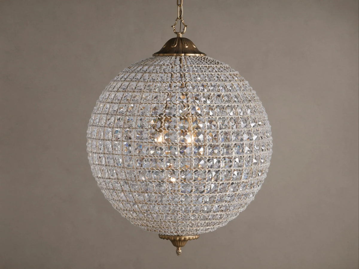 Poppy Chandelier, a glowing spherical fixture of clear multifaceted crystals on an antiqued brass frame, suspended.
