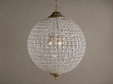 Poppy Chandelier, a glowing spherical fixture of clear multifaceted crystals on an antiqued brass frame, suspended.