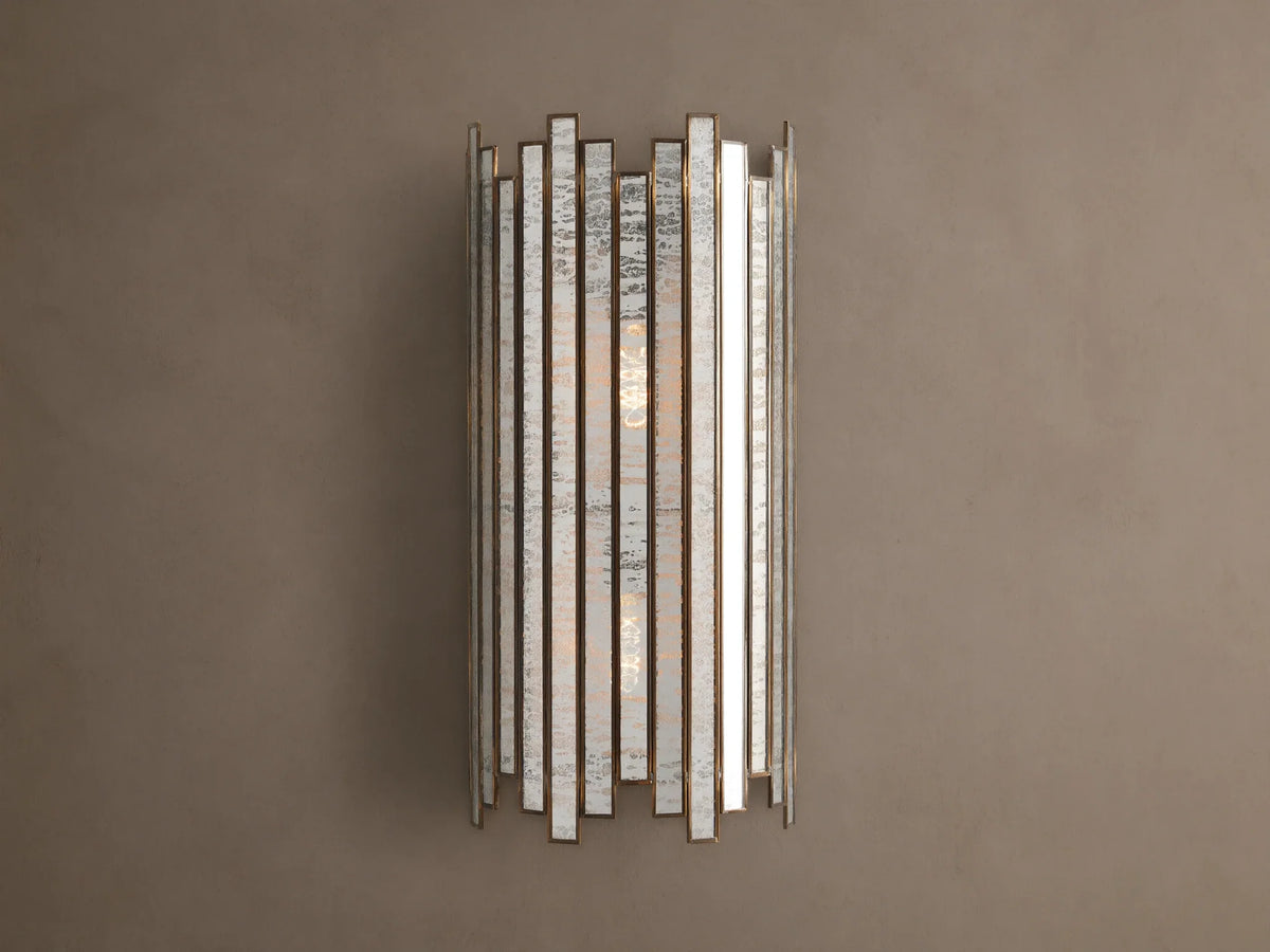 Laila Sconce: vertical antique copper frame with rectangular antiqued mirrored-glass panels, glowing softly against a beige wall.
