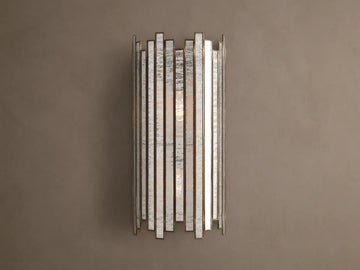 Laila Sconce: vertical antique copper frame with rectangular antiqued mirrored-glass panels, glowing softly against a beige wall.