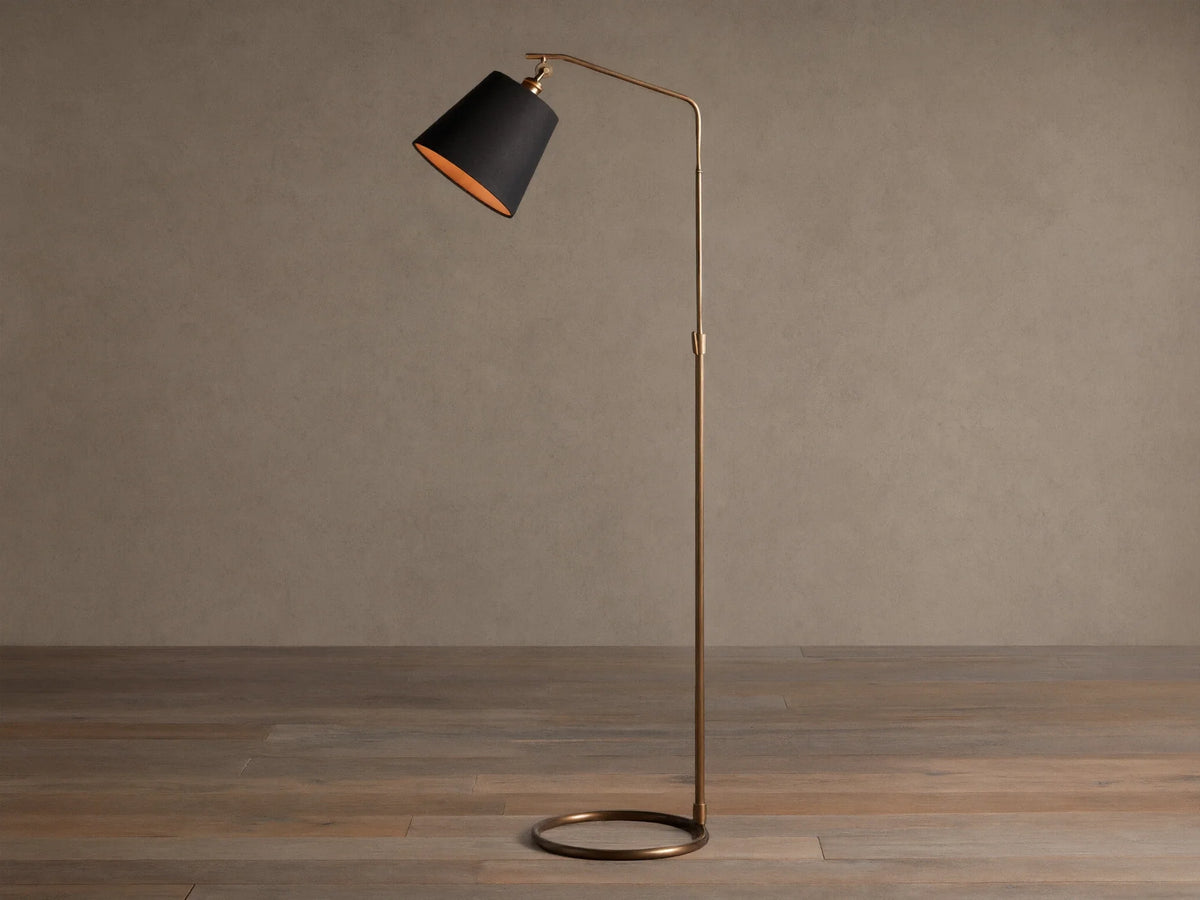 Kellen Antiqued Brass Floor Lamp, slender frame, black fabric shade with warm interior, round base on wooden floor.