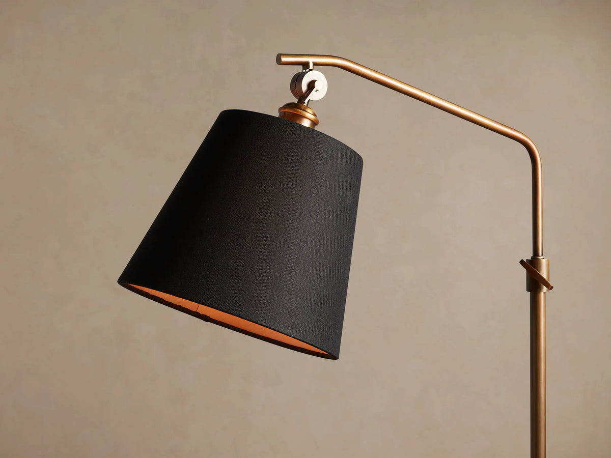 Kellen Antiqued Brass Floor Lamp with a slender, curved antiqued brass stand and black conical shade, warm interior.