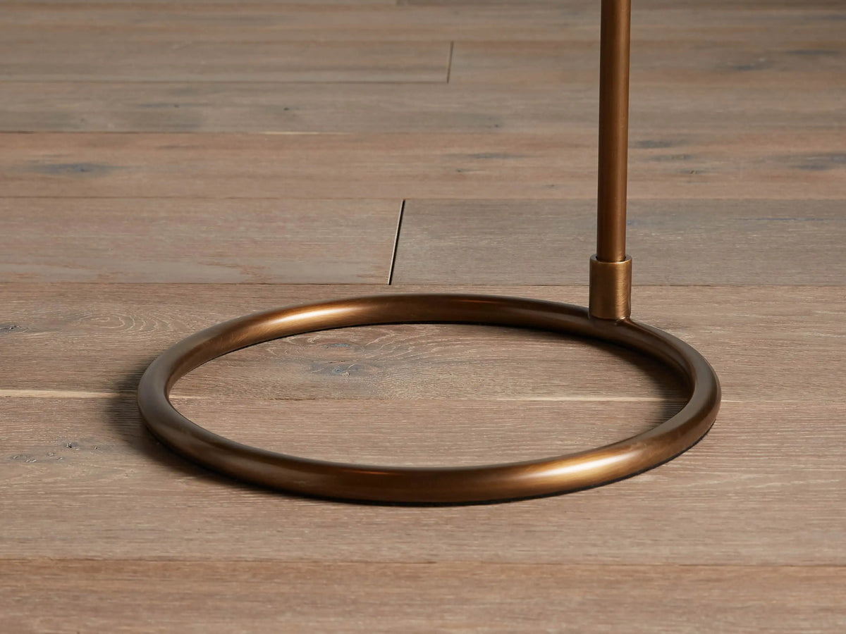 Kellen Antiqued Brass Floor Lamp. Side close-up of its antiqued brass arm & black tapered fabric shade with a warm interior.