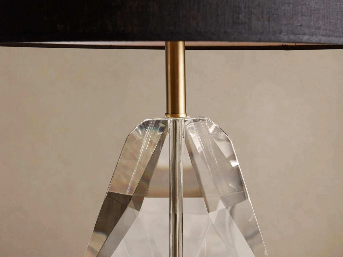 Lola Teardrop Table Lamp with black drum shade, clear faceted crystal base, and brass accents, on a wooden table.