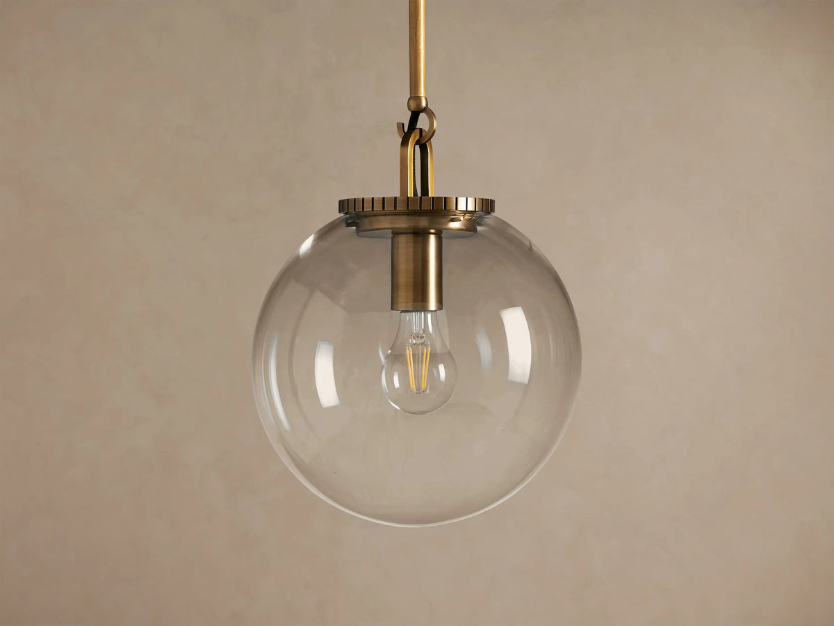 Wescott Globe Pendant: Brass-finished rod and hardware holding a clear glass globe with a filament bulb inside, against a plain wall.