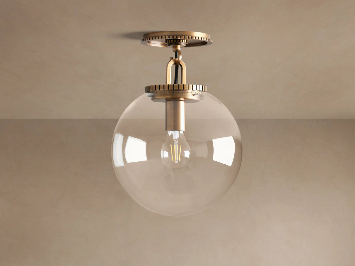 Wescott Globe Flush Mount with a clear glass globe shade, brass hardware, mounted on a ceiling against a neutral wall.
