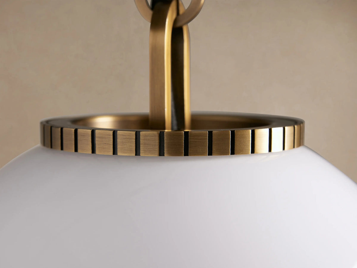 Wescott Globe Pendant. White milk glass globe with brass rod and fittings, hanging centered on a textured beige wall.