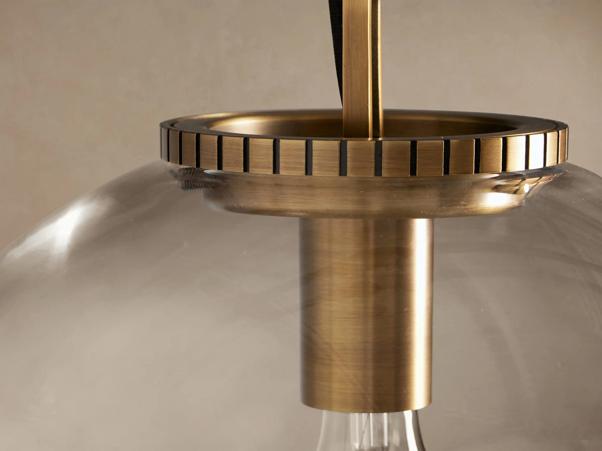 Wescott Globe Pendant. Clear glass globe, brass hardware & chain, light bulb visible inside, hanging against beige wall.