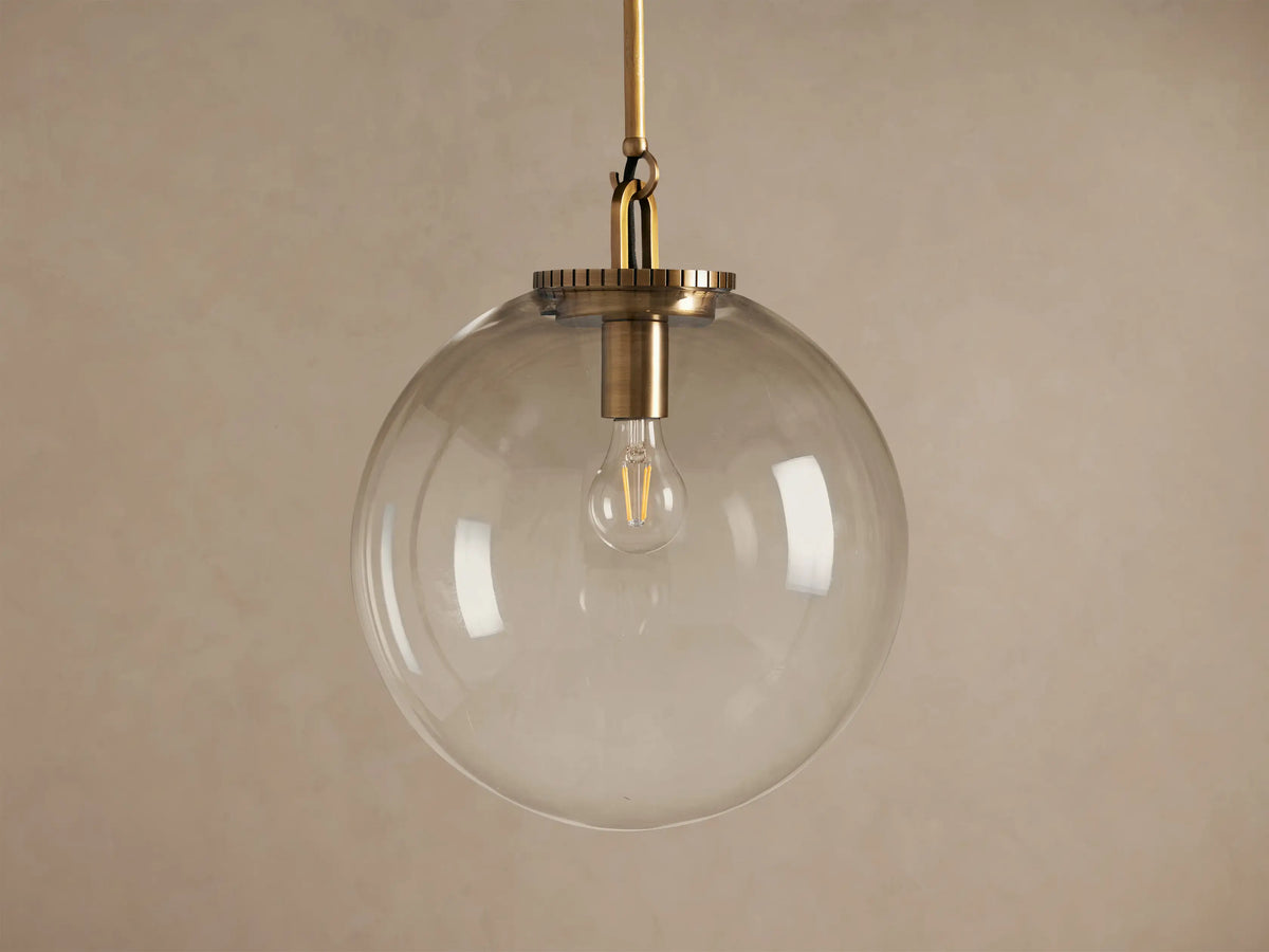 Wescott Globe Pendant: clear glass globe with a brass rod and exposed bulb, hanging against a warm, neutral wall.