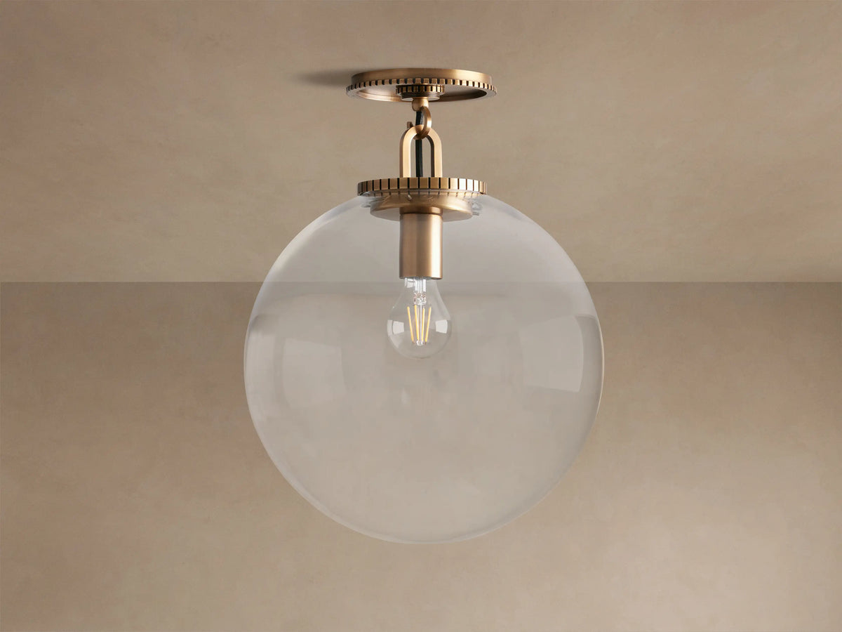 Wescott Globe Flush Mount with brass hardware & large clear glass globe, featuring a filament bulb, mounted on a ceiling.