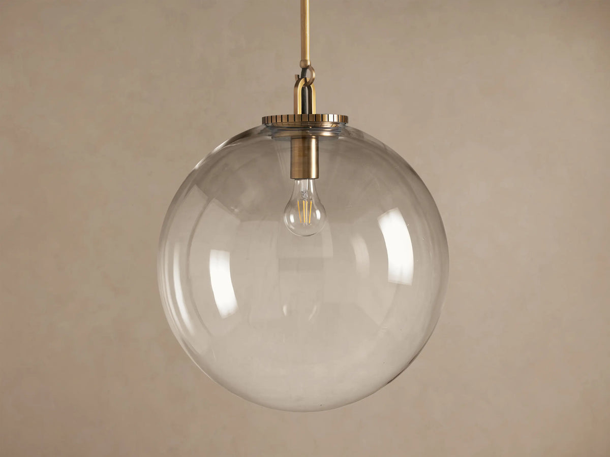 Wescott Globe Pendant with Rod: clear glass globe hangs from a brass rod, revealing a warm glowing filament bulb inside.