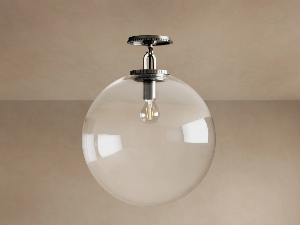 Wescott Globe Flush Mount: clear glass globe, lit Edison bulb, dark bronze mount, metallic stem on a beige ceiling.