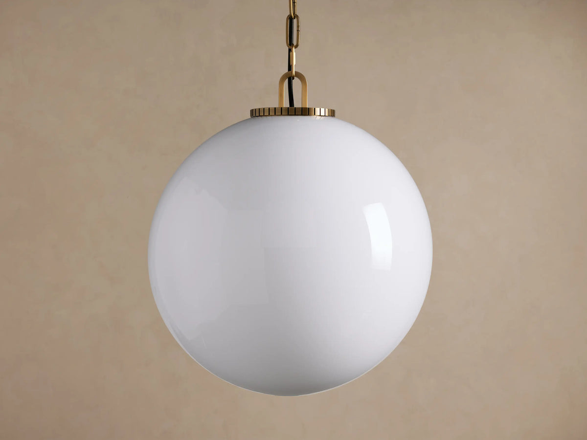 Wescott Globe Pendant with Chain. White milk glass globe pendant light with brass hardware and chain, hanging against a brown wall.