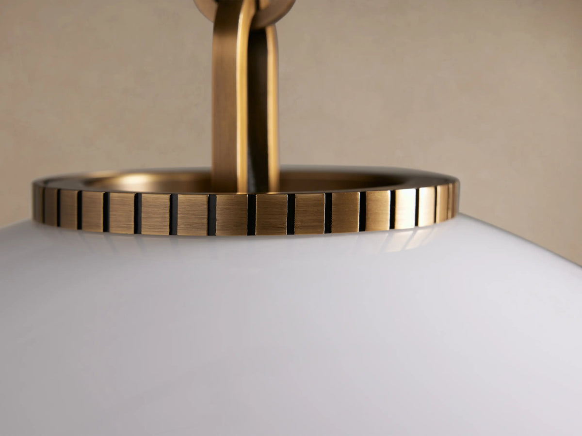 Wescott Globe Pendant: Large, white milk glass globe with brass accents, suspended by a brass chain against a light beige wall.