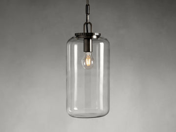 The Wescott Cylinder Pendant features a clear glass cylinder shade with visible filament bulb and brass or bronze fittings, suspended by a chain.