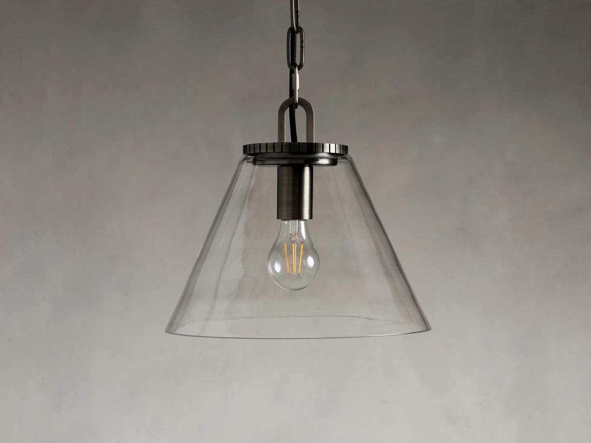 Cone-shaped clear glass pendant light with a visible bulb inside, suspended by a chain and metal fixture against a neutral background.