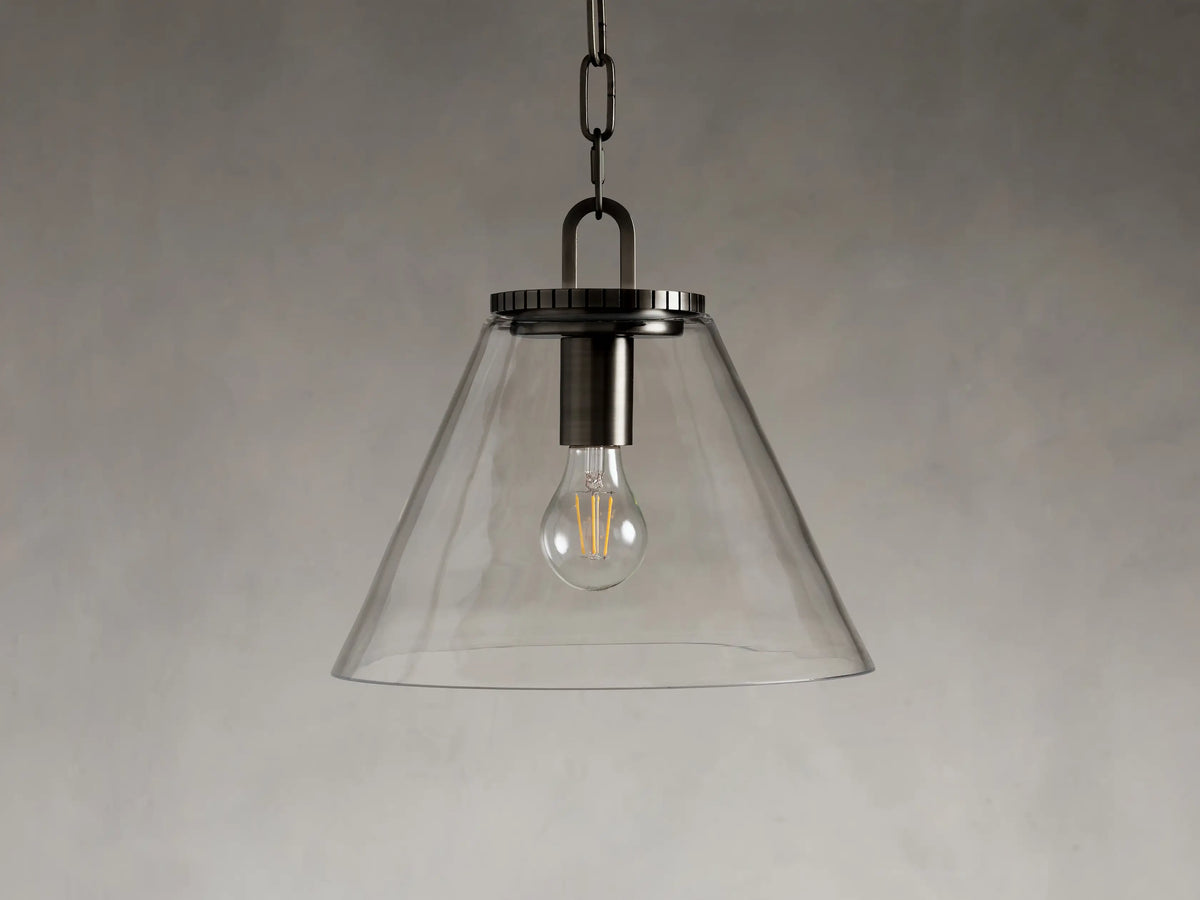 Clear glass cone pendant light with visible bulb, suspended by a dark metal chain against a neutral background.