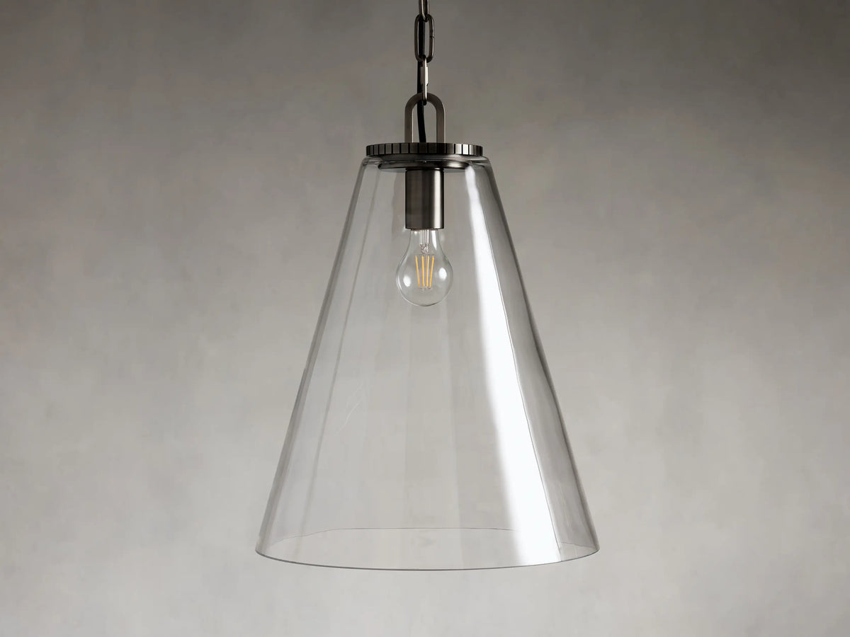 Clear glass cone-shaped pendant light with steel fixture, suspended by a black chain. Single visible bulb interior against a soft gray background.