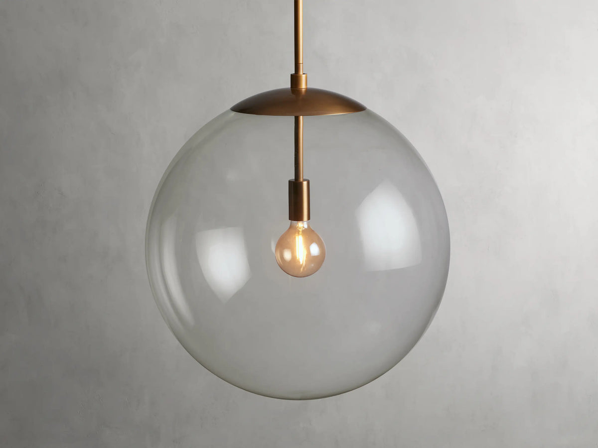 A clear glass globe pendant with a brass finish rod and fixture, showcasing a visible bulb inside, hung against a plain background.