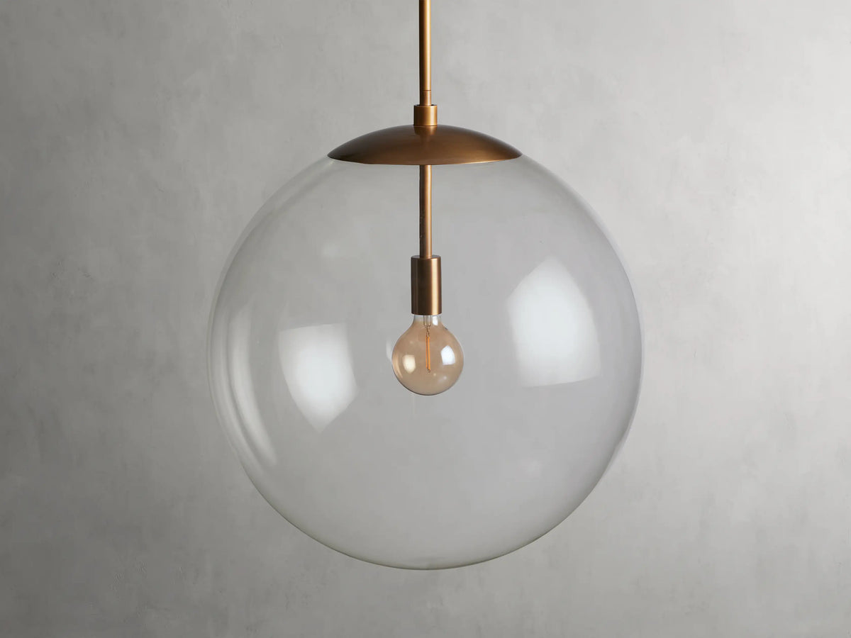 A clear glass globe pendant with a brass finish rod and fixture, showcasing a visible bulb inside, hung against a plain background.