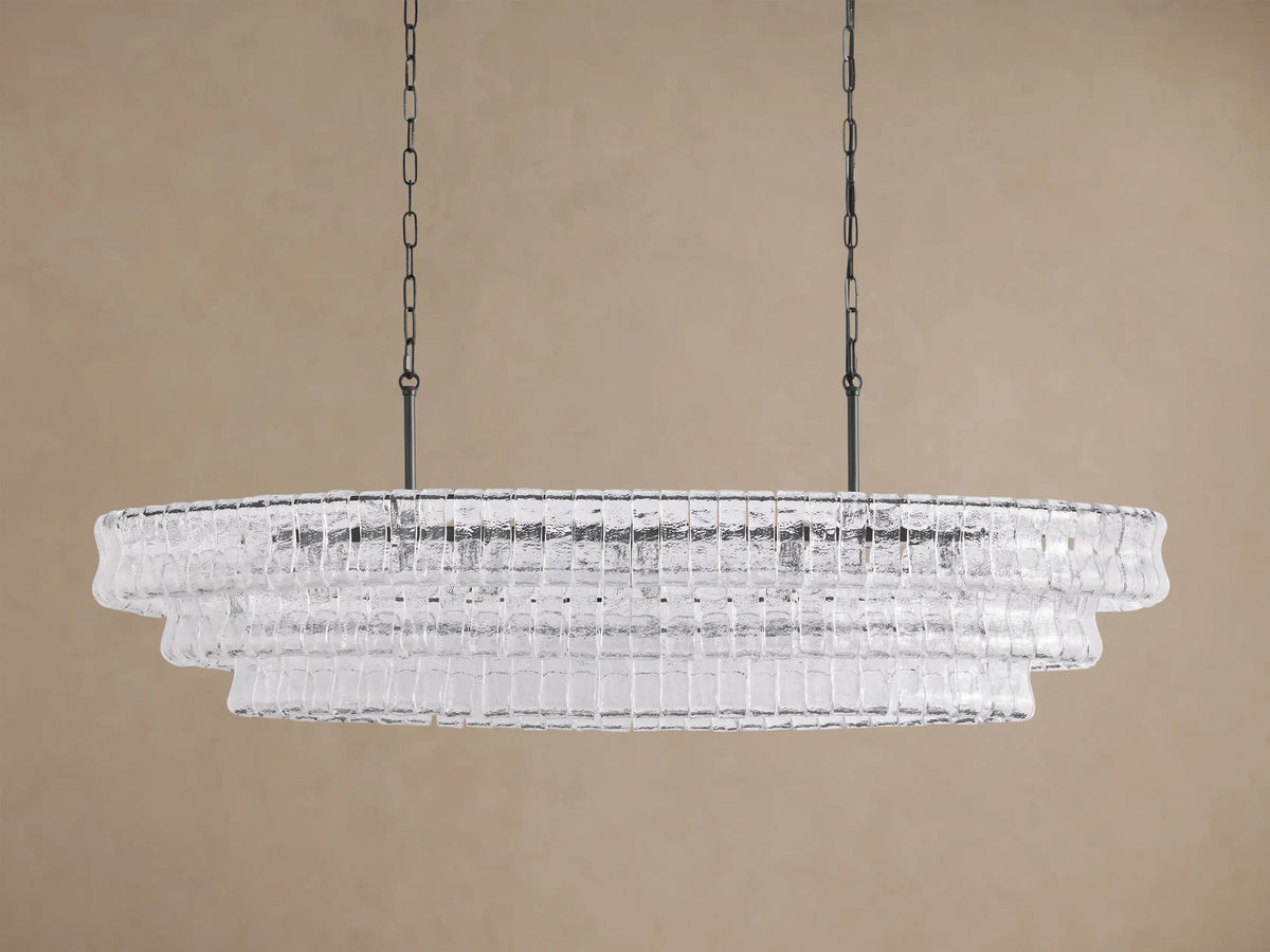 Ghiaccio Oval Chandelier: clear textured glass in tiered wavy segments, suspended by dark chains, with a soft inner glow.