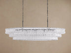 Ghiaccio Oval Chandelier: clear textured glass in tiered wavy segments, suspended by dark chains, with a soft inner glow.