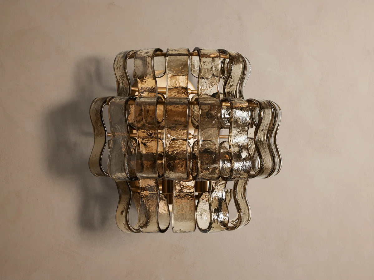 Ghiaccio Sconce: layered amber textured curved glass wall light emitting a warm glow on a neutral background.