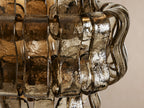 Ghiaccio Sconce, a wall-mounted light with wavy, textured smoky amber glass panels over a brass-toned frame on a neutral wall.