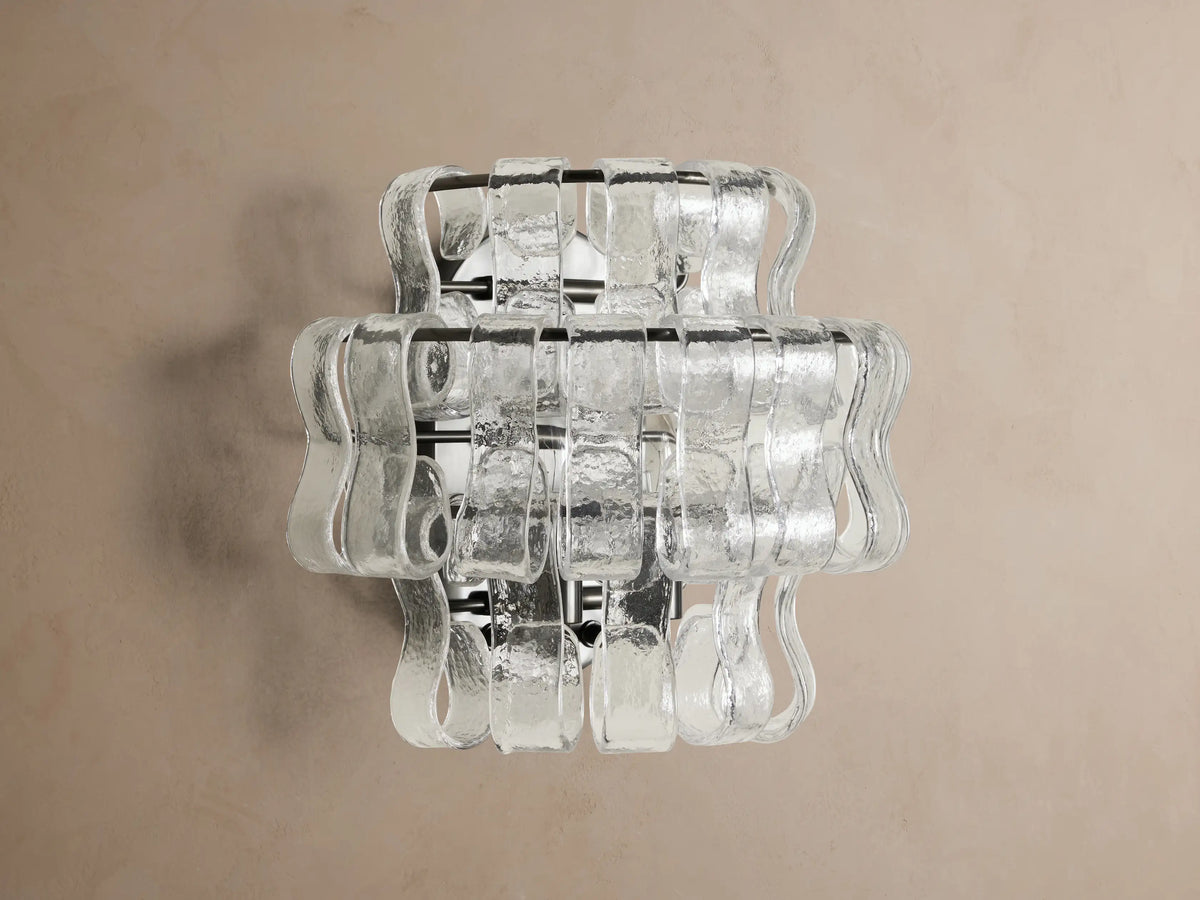 Ghiaccio Sconce with wavy, layered, textured clear glass panels resembling ice, illuminated on a wall.