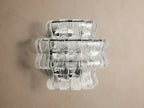 Ghiaccio Sconce with wavy, layered, textured clear glass panels resembling ice, illuminated on a wall.
