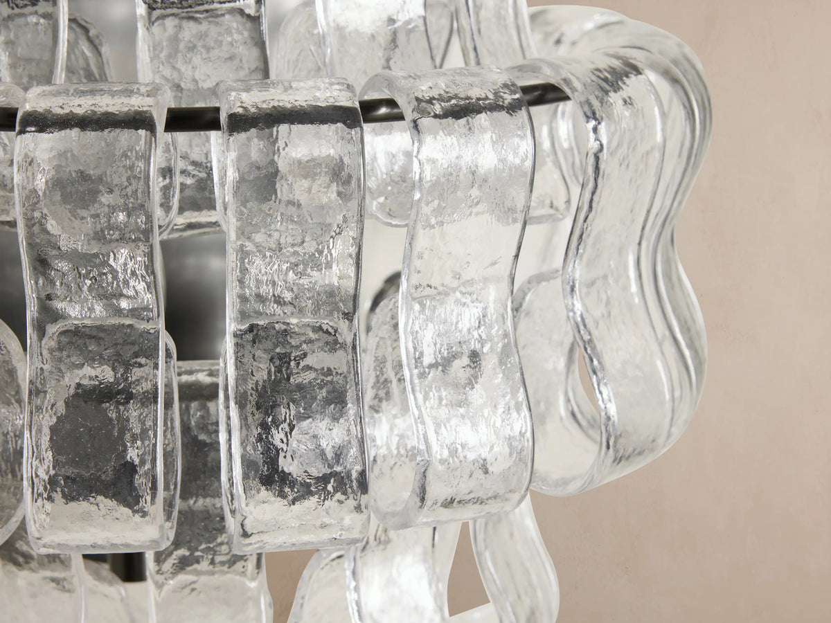 Ghiaccio Sconce: A wall-mounted light with wavy, textured clear glass panels arranged in horizontal layers on a metallic frame.