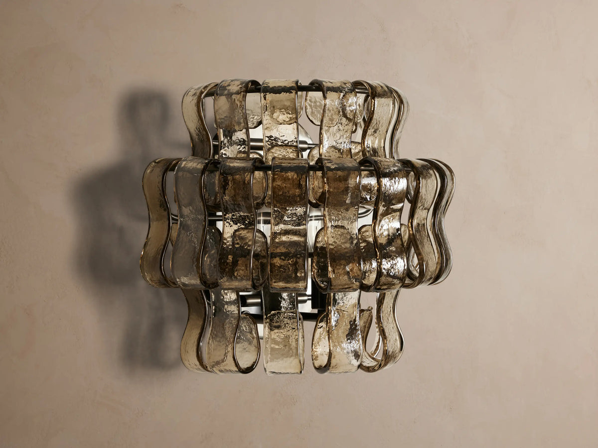 Ghiaccio Sconce, wall-mounted, features layered wavy textured smoky glass and a dark steel frame, glowing warmly.
