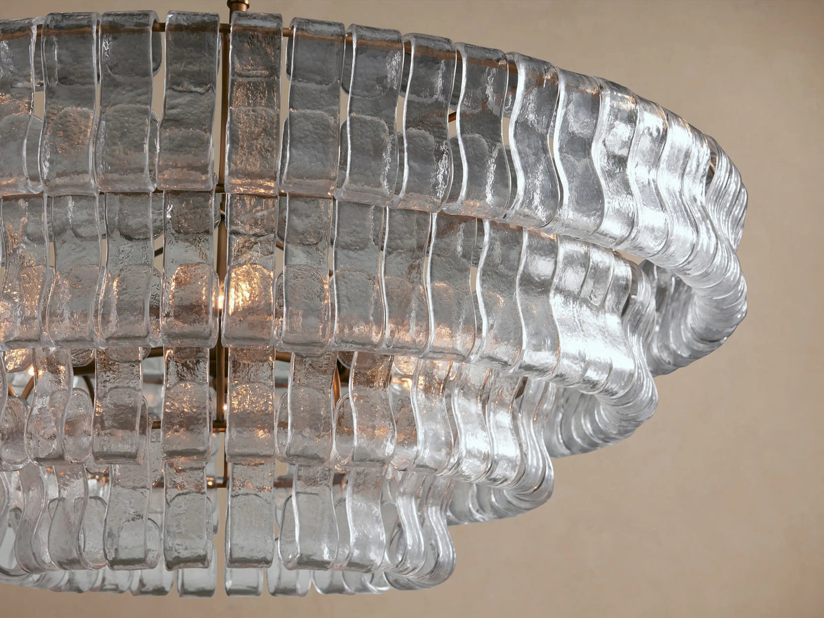 Close-up of Ghiaccio Round Chandelier with clear, textured curved glass strips forming wavy rings, warm light glowing from within.