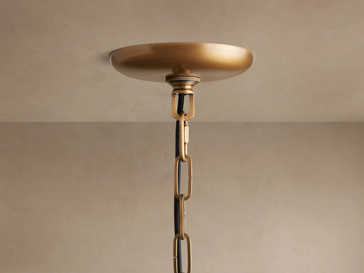 Close-up of Ghiaccio Round Chandelier's brass ceiling canopy, connecting to a chain with black cord, against a light ceiling.