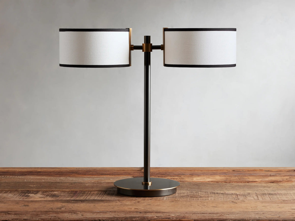 Daphne 2-Light Table Lamp with black-finished base and two white linen shades with black trim on a wooden surface.