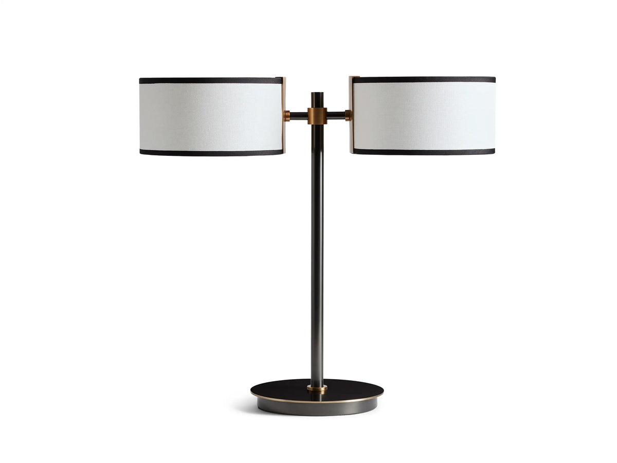 Two-light table lamp with bronze base, featuring dual white linen shades with black trim. Positioned on a wooden surface.