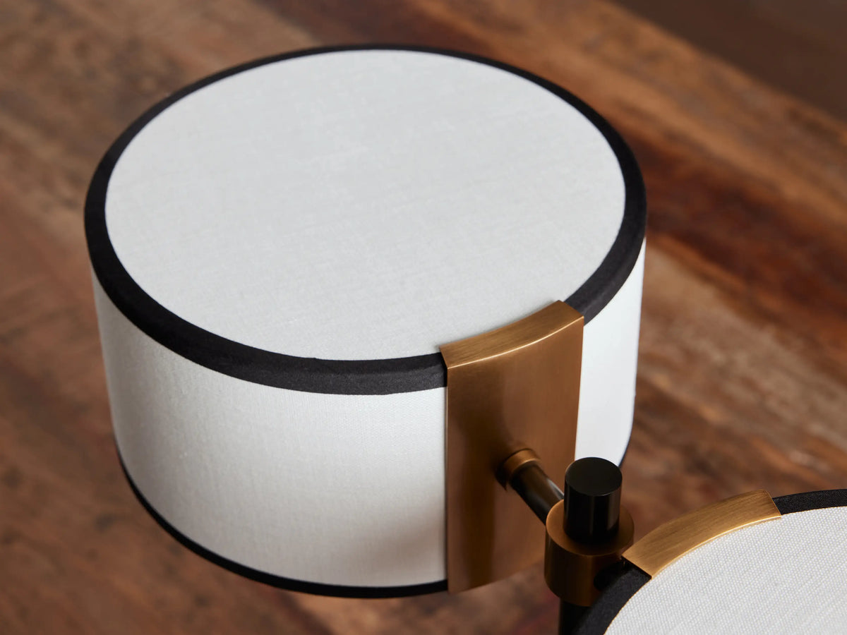 Daphne table lamp with two white drum shades trimmed in black, black metal base and stem, central gold accents, on a white background.