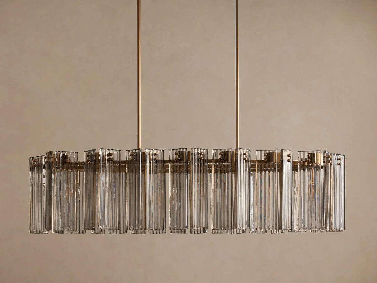 Delsie Oval Chandelier: large oval light fixture with clear fluted glass rods and a burnished brass frame, hanging from two rods.