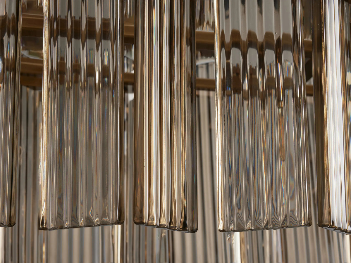 Close-up of Delsie Oval Chandelier's clear, ribbed glass rods hanging vertically, with warm brass-toned metal in the background.