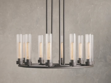 Andreas 10-Light Round Chandelier with a bronzed steel frame, featuring ten vertical, tubular clear glass shades. Mounted against a textured grey wall.