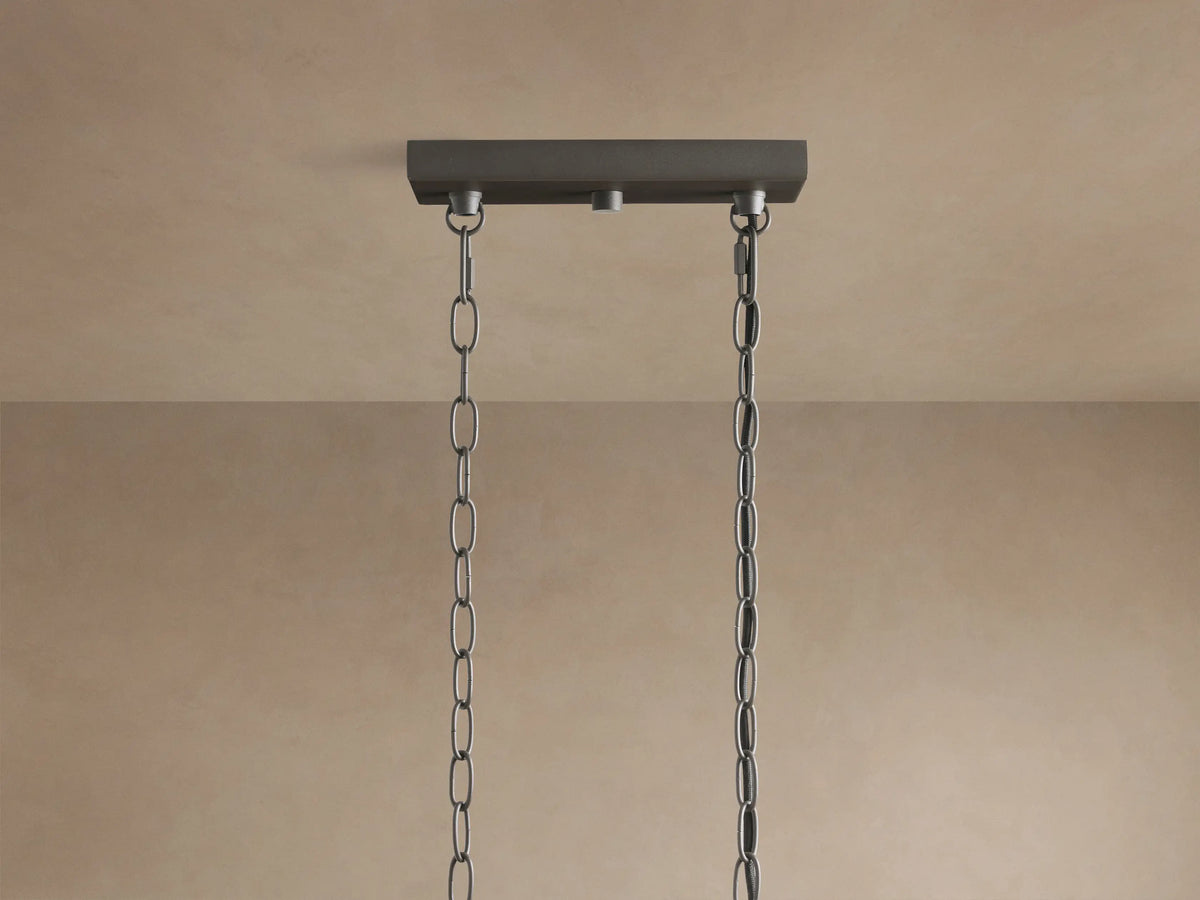 Close-up of Andreas Linear Chandelier: dark metal frame holding five ribbed clear glass shades with glowing Edison bulbs.