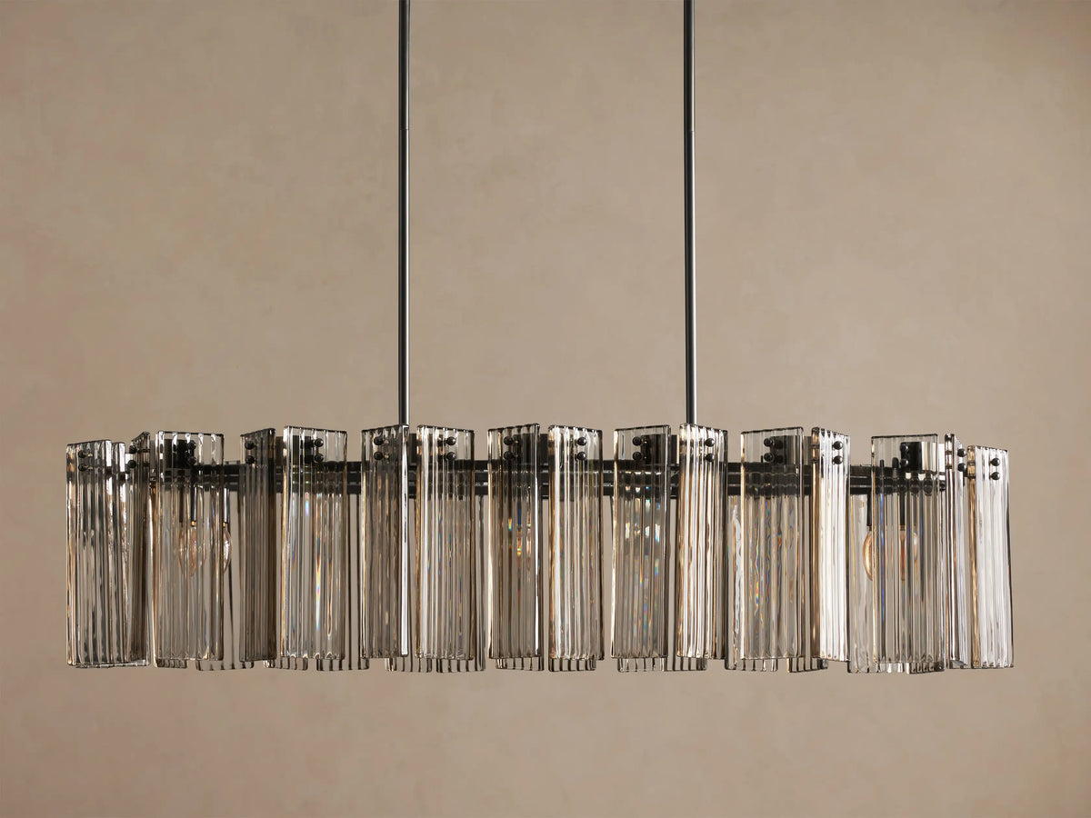 Delsie Oval Chandelier: Dark bronze steel frame with multiple clear fluted glass panels, suspended against a plain wall.