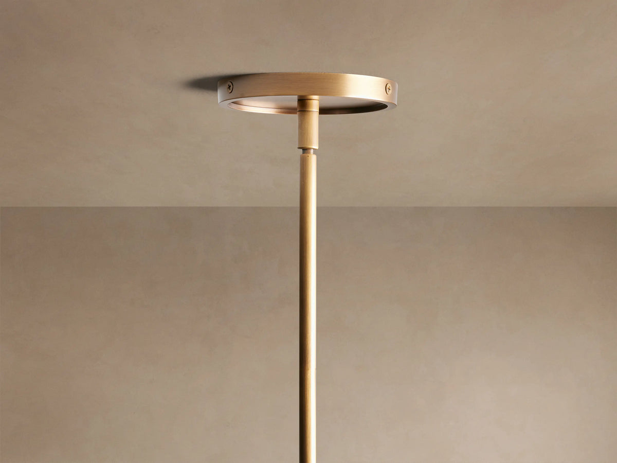 Close-up of Theron Linear Chandelier with warm brass finish, clear conical glass shades, and glowing filament bulbs.