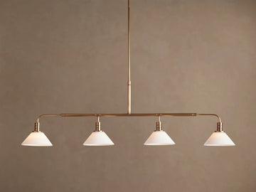 Theron Linear Chandelier with four milk glass cones on a horizontal brass bar, suspended against a warm brown wall.