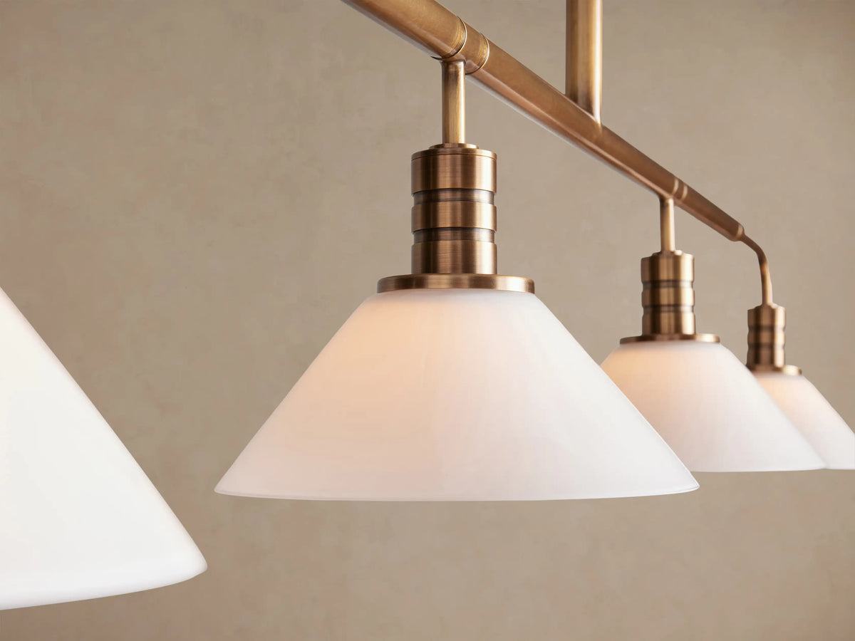 Theron Linear Chandelier, brass finish, four white conical milk glass shades on a horizontal bar, hanging from a vertical rod.
