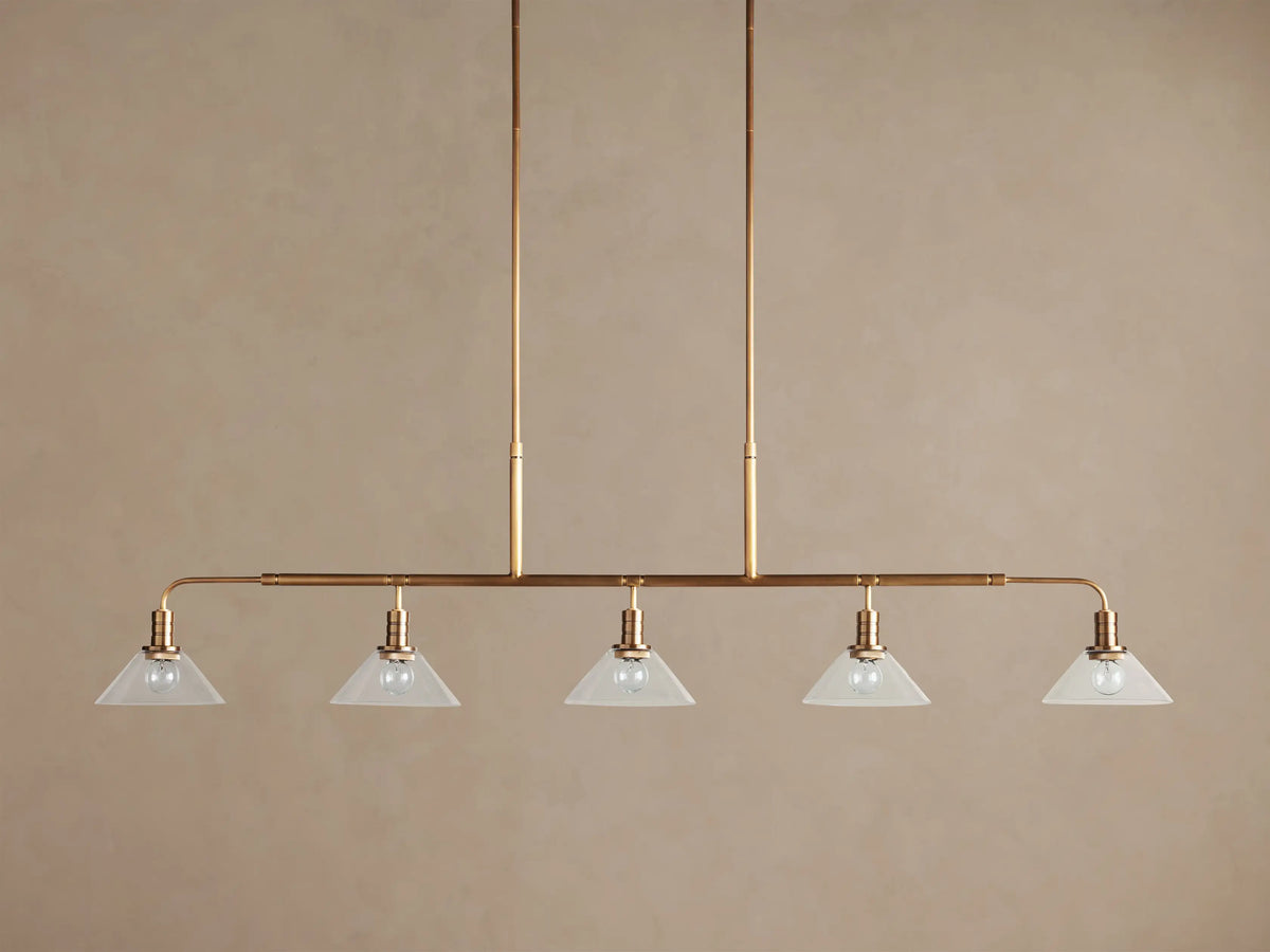 Brass Theron Linear Chandelier, 5 inverted milk glass cone shades with lit bulbs, suspended from vertical rods.