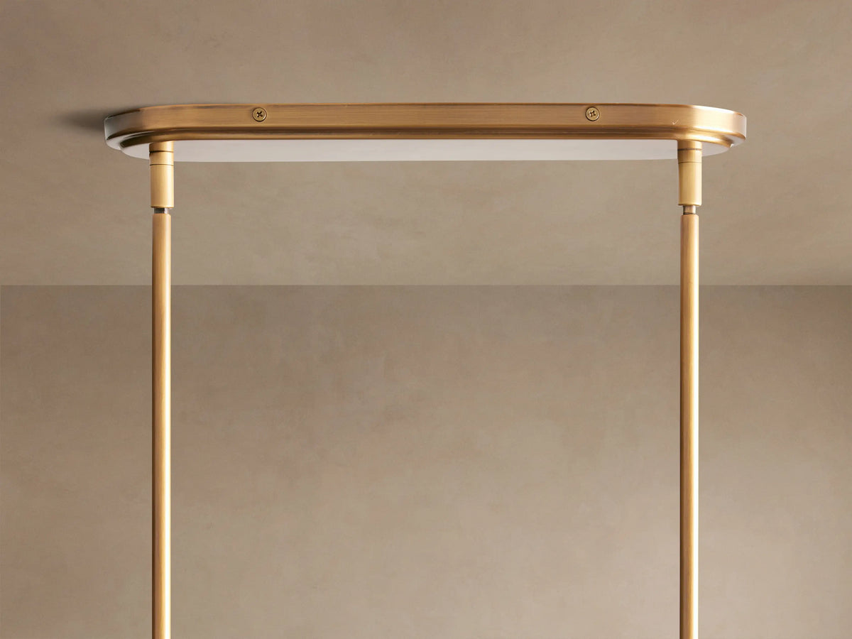 Close-up of a brass-finished Theron Linear Chandelier with clear cone glass shades and glowing bulbs against a light wall.