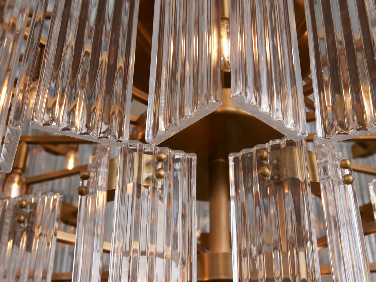 Delsie Round Chandelier with clear glass rods in a tiered design and burnished brass accents, hanging against a neutral wall.