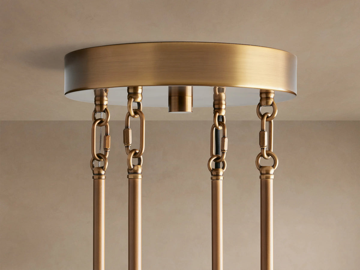 Close-up of Delsie Round Chandelier. Clear, fluted glass panels are attached to a burnished brass frame with warm light.
