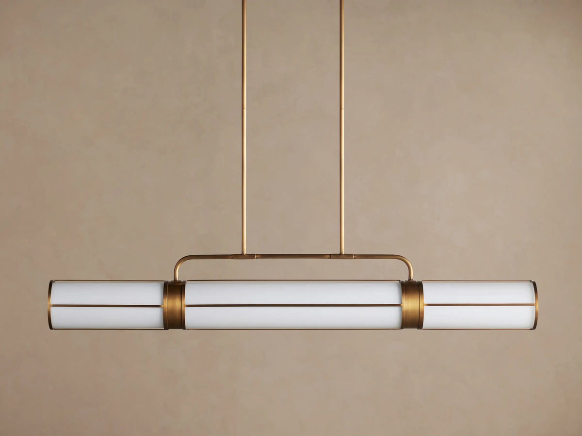 Remming Linear Chandelier: Three glowing milk glass cylinders in a burnished brass frame, suspended from above.